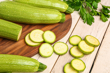 Board with many fresh green zucchini and parsley on white wooden background