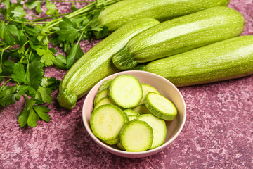 Many fresh green zucchini and bowl with slices on purple background