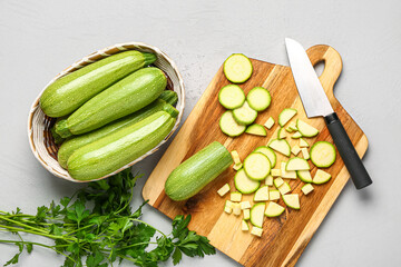 Plakat Wicker bowl with many fresh green zucchini and board of slices on grey background