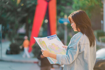 Young tourist woman searching right direction on map. Positive smiling young female tourist searches for inspiring places.  holds paper map, finds new sightseeing for discovering.
