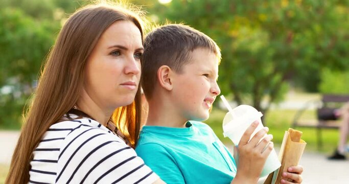 Child and mom have fun in the park, child eats hotdog and drinks milkshake.