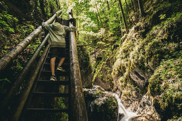 View of boy climbing the steps of a wooden walkway next to white water cascading down the Dr. Vogelgesang-Klamm gorge in Spital am Pyhrn, Austria © schusterbauer.com