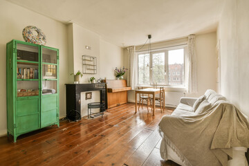 a living room with wood flooring and a green cabinet in the center of the room is a small dining table