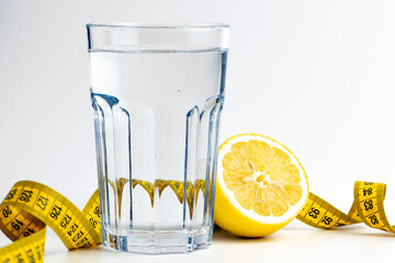 a glass of water with a lemon and a measuring tape. the concept of diet and proper nutrition