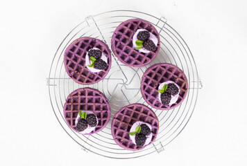 Vegan Purple soft round waffles with cream and blackberries. Waffles with the addition of blackberry puree. On a serving metal stand. White background. Top view