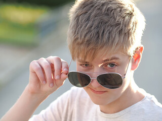 Outdoor portrait of a friendly caucasian blue-eyed teenager in  sunglasses - 608820346