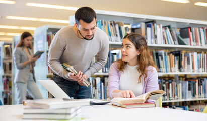 Fototapeta premium Young woman and man working with laptop and books, finding information at library together