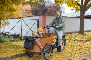 Mature happy father with a child riding cargo bicyclein countryside 