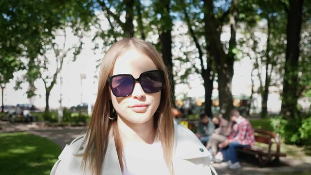close portrait of a young woman wearing sunglasses who are walking in the city park 4k