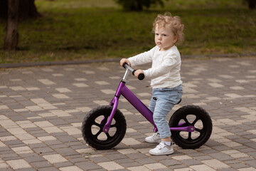 Cute little smiling child learning to ride a balance bike in the park