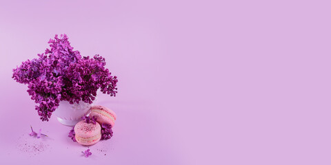Pastel colored sweet french macaroons with lilac flowers on pink background. Beautiful composition for bakery and pastry shop, copy space for text