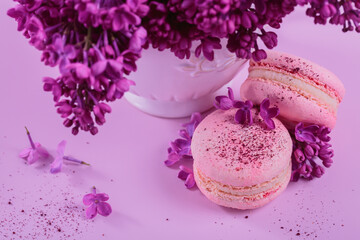 Close up of Pastel colored sweet french macaroons with lilac flowers on pink background. Beautiful composition for bakery and pastry shop