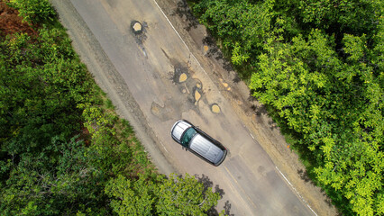 AERIAL TOP DOWN: Careful driving of car that tries to avoid dangerous road pits - obrazy, fototapety, plakaty