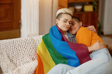 Young freedom lesbian woman cuddling in lgbt rainbow flag while sitting on sofa