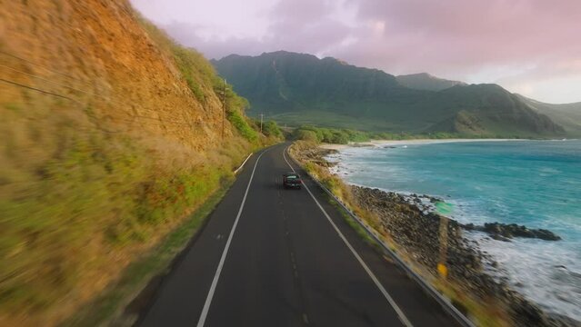 Tourists traveling by Oahu island Hawaii USA. Car driving along cinematic coastline. Aerial road above dramatic rocky ocean shore towards green volcanic mountains. Background of Happy summer vacation