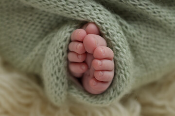 Tiny foot of a newborn. Soft feet of a newborn in a green, pistachio, olive woolen blanket on a white flaccati background. Macro photo of the toes, heels and feet of a newborn.