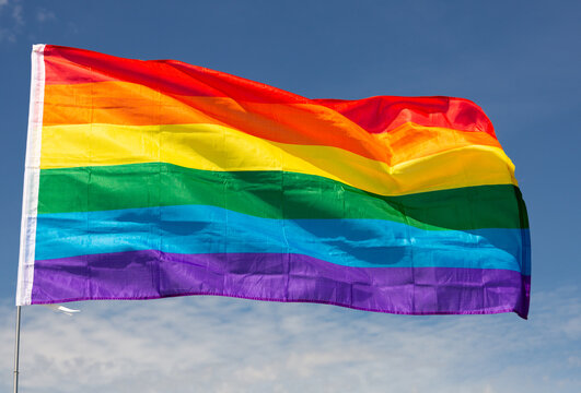 Huge flag of LGBT attached on long handle against background of clear bright sky