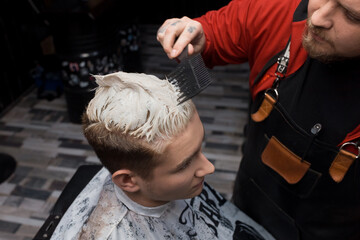 The hand of a professional barber with a comb will check the degree of coloring of the client's hair in the hairdresser at work