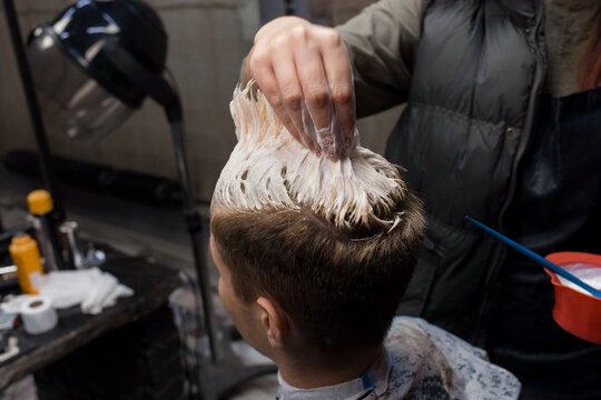 The hand of a professional hairdresser's girlfriend touches and dyes the client's boyfriend's hair white in a hairdresser or barbershop