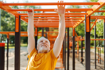 Obraz premium Handsome self determines senior man doing pull ups exercise on crossbar on summer sportsground