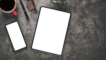 Dark office desk workplace with blank screen tablet and smartphone, laptop, keyboard, pen, eyeglass and notebook, Top view flat lay..