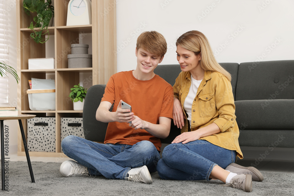 Sticker Happy mother and her teenage son with phone spending time together on floor at home