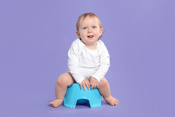 Little child sitting on baby potty against violet background