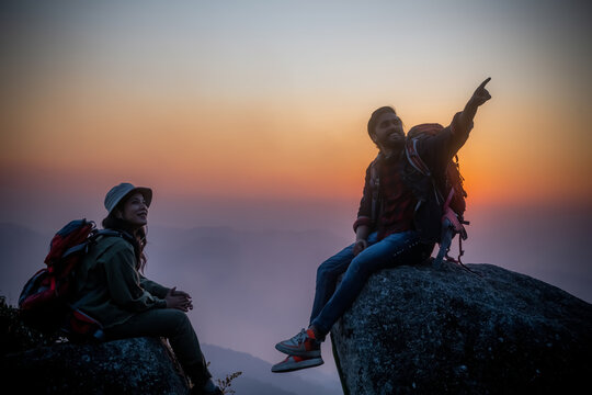 Hikers with backpacks relaxing on top of a mountain and enjoying the view of valley at sunset