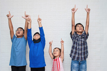 Obraz premium Portrait of cute Asian little kids in casual clothes looking and pointing up, isolated on a white background