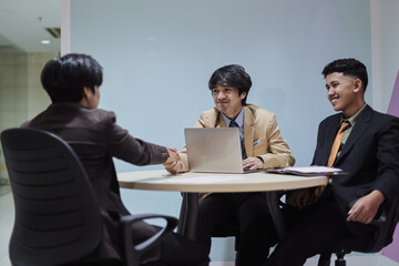 Young Asian businessman smiling and handshaking with partner after successful negotiations or job...