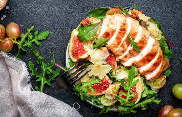 Gourmet salad with fresh figs, grilled chicken, parmesan cheese, grape, arugula, swiss chard with wine vinegar dressing. Black kitchen table background, top view