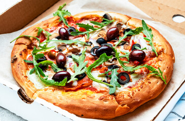 Hot Pizza in box with salami sausage, mozzarella cheese, mushrooms, black olives, spicy tomato sauce and arugula, white table background, top view