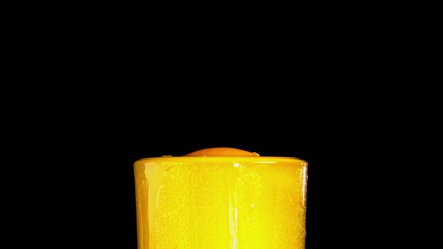 orange slice falling into orange juice glass and making splashes and siking smoothly  - close up- with black background
