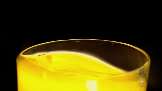 ice qube falling into orange juice glass with a black background
