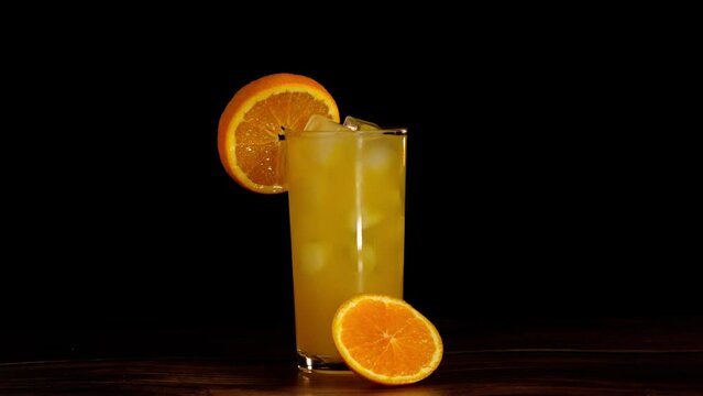 orange juice glass with a slice of orange on top with a black infinit background