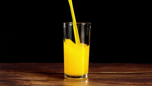 pouring fresh orange juice into aclear glass on a wooden table with a black background