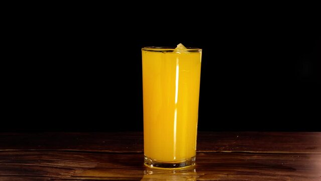 ice qube falling into orange juice glass and making splashes slow motion with black background