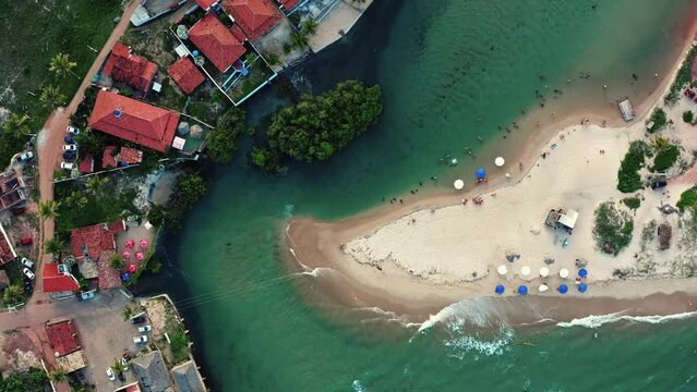 Wide aerial drone bird's eye top view of the tropical turquoise Catu river where it combines with the sea with tourists swimming in the beach town of Sibauma, Tibau do Sul, Rio Grande do Norte, Brazil