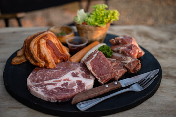 Sliced raw pork meat and sausage on black plate.