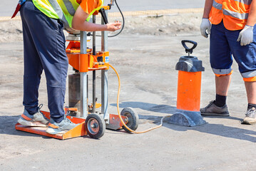 Road builders set up a gasoline drilling machine to cut asphalt concrete samples on a sunny day.