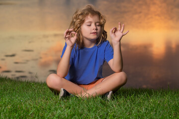 Child with close eye mindfulness meditating, sit on grass for peace and yoga. Kid relax on summer sunset. Freedom and carefree kids concept.