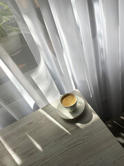 A cup of coffee on the table near the window. Bright sunlight