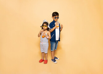 Indian kids drinking cold drink, Little boy and girl drink soda or soft drink through straw isolated over beige background.