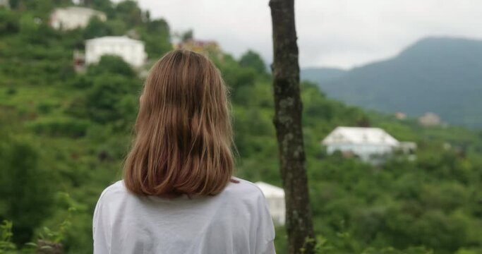 Tourist girl hiker hiking in mountain valley admiring nature, rear view. Explorer trekking in hills covered gren plants. Traveler has adventures. Wanderlust travel tourism vacation journey concept.