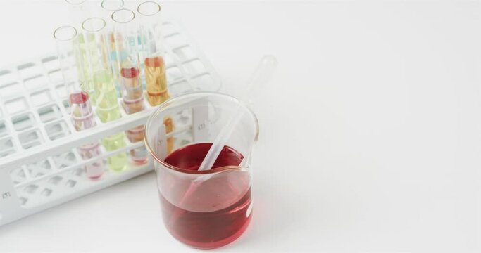 Coloured liquid in flask with test tubes in stand on white background with copy space, slow motion
