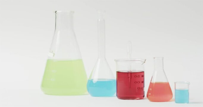 Coloured liquids in flasks on white background with copy space, slow motion