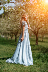 Fototapeta premium Blond garden. Portrait of a blonde in the park. Happy woman with long blond hair in a blue dress.
