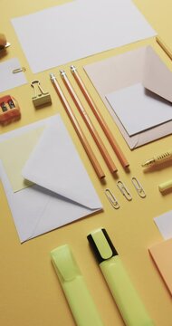 Vertical video of close up of pencils and stationery arranged on yellow background, in slow motion