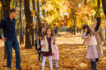Naklejka premium portrait of a big family in autumn city park, happy parents and children playing together and throwing yellow leaves, beautiful nature, bright sunny day