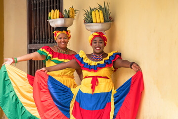 Two cheerful fresh fruit street vendors aka Palenqueras in the Old Town of Cartagena, Colombia.  - obrazy, fototapety, plakaty